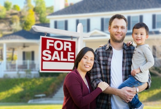 man, woman, and child standing in front of home with for sale sign