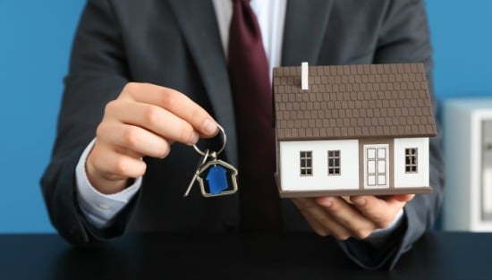 man in suit holding keys and model house - real estate market concept
