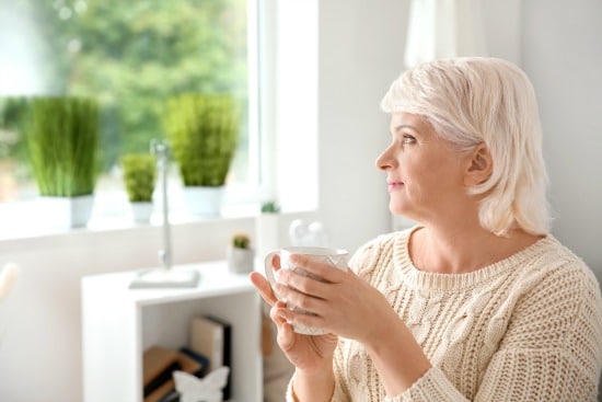 woman looking out window while holding coffee cup