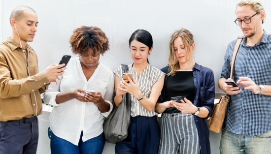 5 people standing against a wall looking at their cell phones