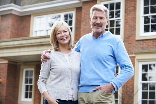 woman and man smiling and standing in front of a home.
