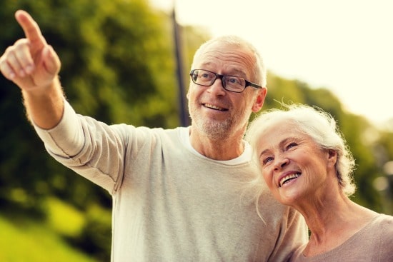 senior man looking off into distance and pointing while standing beside senior woman