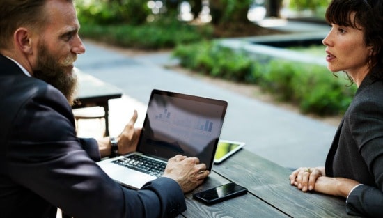 man with credit report information on laptop screen sitting at table talking to woman