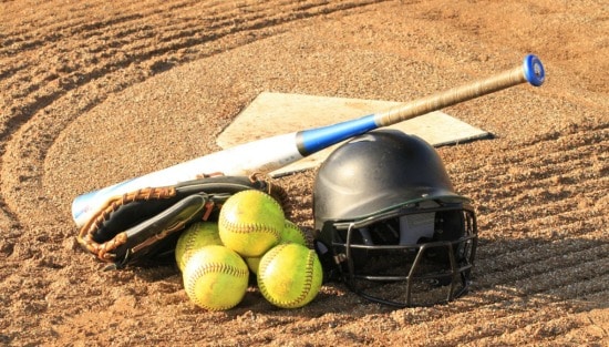 softballs, baseball glove, bat, helmet, and base on a dirt field